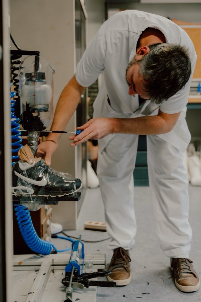 Prothésiste appliquant la résine de stratification sur une prothèse de jambe chaussée, dans l'atelier d'appareillage de l'INI