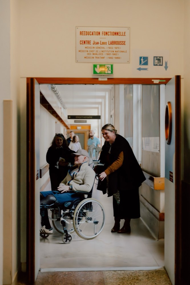 Une soignante accueille en souriant un patient en fauteuil à l'entrée du centre de rééducation Jean-Louis Labrousse