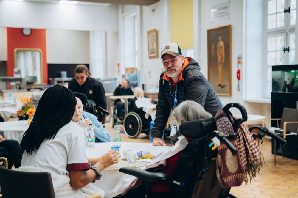 Un visiteur échange chaleureusement avec des pensionnaires réunis autour d'une table dans la salle commune de l'INI